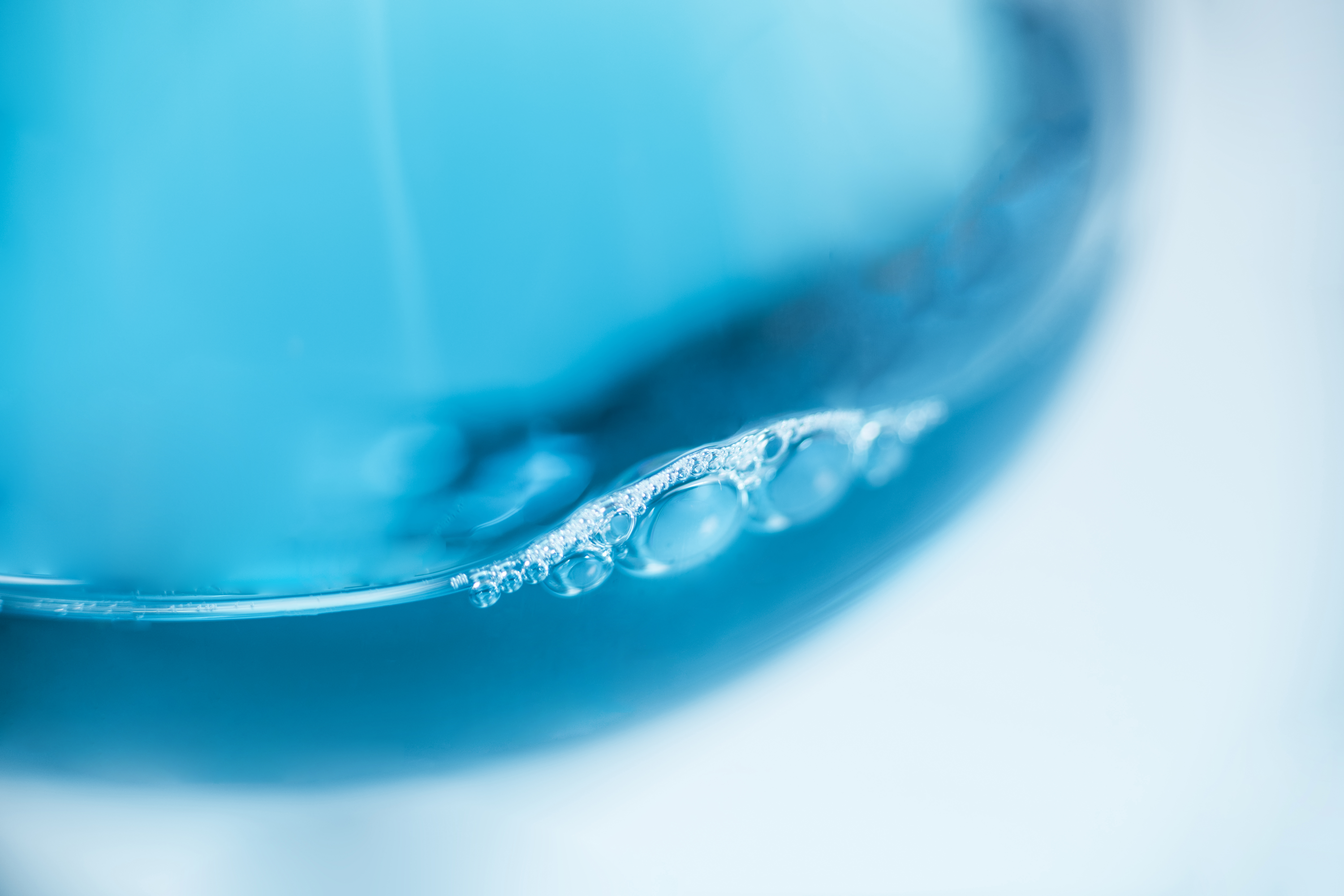 A close-up image of a laboratory beaker that has blue bubbles in it.
